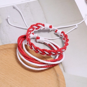 Détail de bracelets d'amitié tressés rouges et blancs avec nœuds réglables sur plateau bois