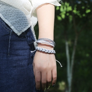 Détail de bracelets tressés à la main en gris et blanc portés au poignet d'un modèle