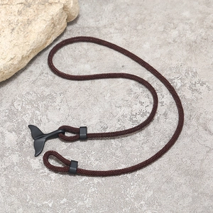 Dettaglio di un bracciale intrecciato marrone con ciondolo a coda di balena nero opaco su pietra