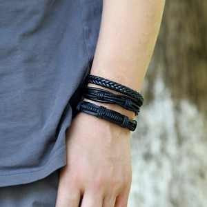 Detail shot of a three-piece set of men's black braided leather bracelets on a wrist
