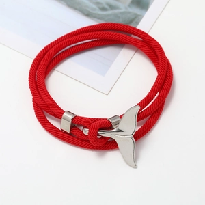 Dettaglio macro di un bracciale intrecciato rosso con ciondolo a coda di balena argento