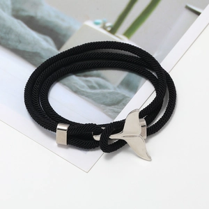 Dettaglio di un bracciale in corda intrecciata nera con ciondolo a coda di balena d'argento