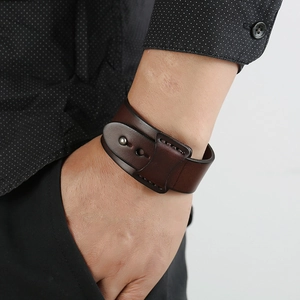Bracelet vintage en cuir marron foncé avec clous en métal et coutures au poignet d'un homme