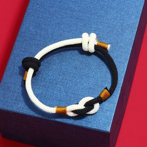 Detail of hand-woven black and white rope bracelet with golden silk thread knot