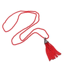 Close-up of a long beaded necklace featuring a vibrant red tassel and dark metal hardware