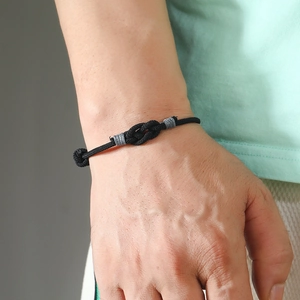 Close-up of a hand-woven black minimalist knot bracelet on wrist with gray silk accents
