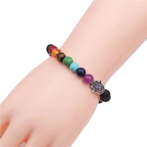 Detail of 8mm lava rock chakra bracelet with Hamsa hand charm and Evil Eye on a wrist