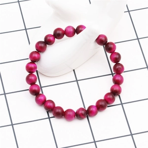 Detail of 8mm magenta tiger eye beaded bracelet showing natural texture on white model