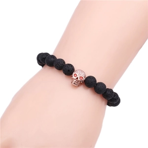 Detail of lava stone bead bracelet with rose gold skull charm and red gemstone eyes