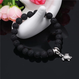 Bracelet en pierre de lave noire avec breloque tortue argentée sur socle réfléchissant