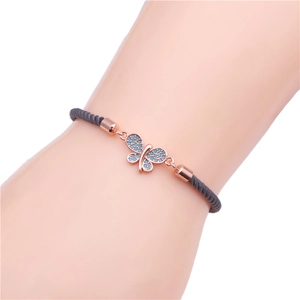Macro shot of rose gold butterfly charm with blue stones on a grey braided rope bracelet