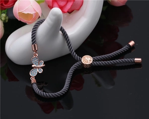 Detail of rose gold butterfly charm with blue stones on grey braided adjustable bracelet