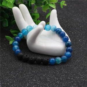 Detalle de cuentas de ágata azul de 8mm y piedra de lava negra en un soporte de mano de cerámica
