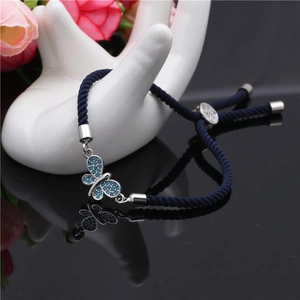 Detailed close-up of blue braided rope bracelet with zircon butterfly charm on white hand model
