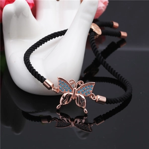 Macro shot of rose gold butterfly charm with blue inlay on black braided rope bracelet