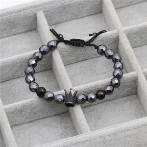 Macro detail of faceted black stone beads and a zircon crown pendant on a beaded bracelet