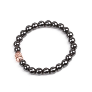 Detailed view of hematite beaded bracelet with rose gold Buddha head charm on white surface