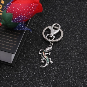 Close-up of silver metal gecko keychain with iridescent abalone shell inlay on black surface