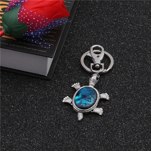 Detail of a turtle keychain with iridescent blue abalone shell on a black textured surface