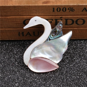 Broche cygne en nacre rose et abalone aux textures irisées sur fond de sable foncé
