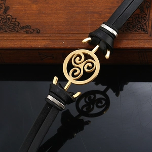 Vintage black leather bracelet with golden Triskelion pendant on a rustic wood background