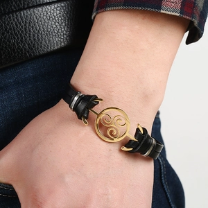 Men's black braided leather bracelet with golden Celtic Triskele charm on a wrist
