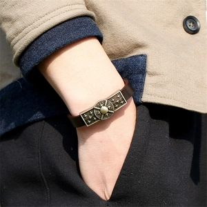 Détail d'un bracelet en cuir marron avec reliefs soleil en bronze porté au poignet