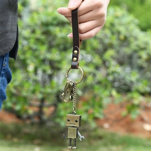 Porte-clés robot rétro en alliage avec bracelet en cuir marron tenu sur fond naturel