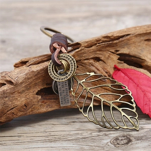 Vintage leaf-shaped leather keychain with bronze hollow design on rustic wood background