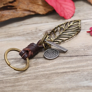 Vintage leaf leather keychain with bronze metal pendants on a rustic wooden surface