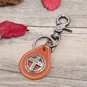 Retro orange leather keychain with cross pendant and metal lobster clasp on wood