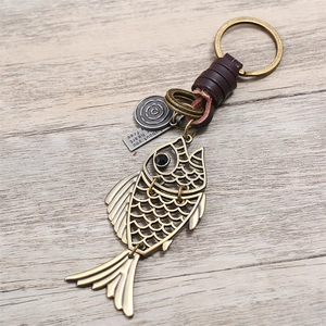 Porte-clés poisson vintage en bronze fait main avec sangle en cuir sur fond de bois clair