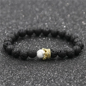 Detail of black lava stone bracelet with white turquoise bead and gold zircon crown charm