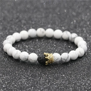 Macro detail of white turquoise beads with a gold crown charm and black lava stone