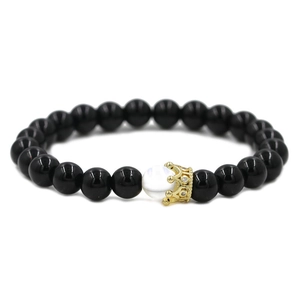 Détail d'un bracelet de perles avec pierres noires, une perle blanche et un charme de couronne dorée
