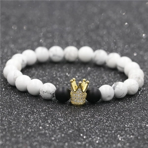 Vue macro de perles en marbre blanc et pierres noires mates avec un pendentif couronne doré