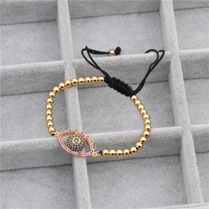 Detail of evil eye charm with pink and blue crystals on golden beaded woven bracelet