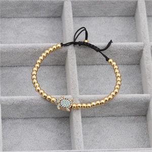 Détail d'un bracelet tissé avec des perles dorées et un pendentif tortue en zircon bleu