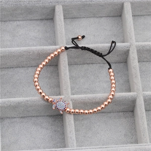 Détail macro d'un bracelet à perles or rose avec breloque tortue bleue sertie de zircons