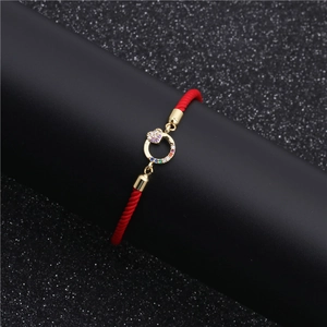 Macro shot of gold-plated red rope bracelet with colorful zircon heart and round charm