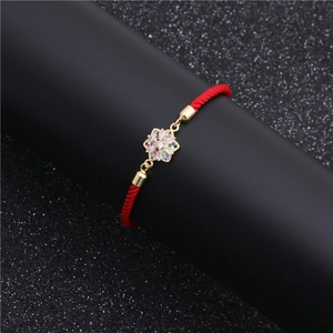 Red cord bracelet with gold flower pendant featuring colorful zircons on a display stand