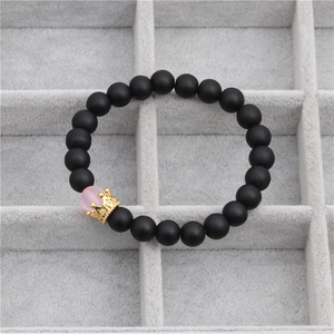 Detailed macro view of matte black beads with a golden crown charm and pink gemstone
