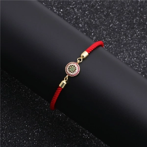 Macro view of red rope bracelet with colorful zircon pavé evil eye charm and gold plating