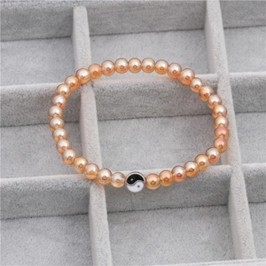 Detail van kralenarmband met amberkleurige parels en een zwarte en witte Tai Chi Yin Yang-bedel