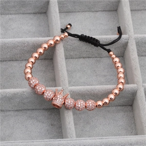 Detail of rose gold crown charm and zircon beads on a woven adjustable black bracelet