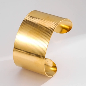 Close-up of golden wide cuff bracelet featuring textured horizontal striped metal details