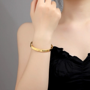 Detailed view of a gold stainless steel bangle with star engravings worn by a model
