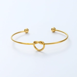 Detailed view of polished gold-plated knot cuff bracelet with smooth solid ball ends