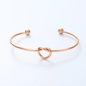 Detail of rose gold knotted open bracelet with polished metal beads on a white background