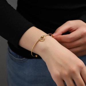 Elegant gold stainless steel heart knot bangle bracelet shown on a female wrist model